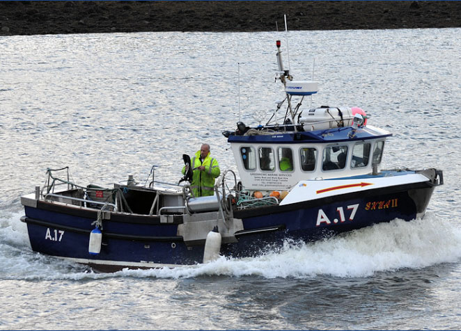 Skua II A17 - Our Kingfisher K26 work boat shown here is a mid-range sized in-shore fishing vesse. One of the most popular sized vessels with in-shore fishermen in the UK. Our Fishing Charter & Day Hire boat makes light work of the Aberdeen sea harbour entrance chop returning to Aberdeen Harbour with a compliment of crew in the wheelhouse. The image shown here also shows (1) crewman mending nets in the ample space of the rear open deck of the boat wearing regulation high visibility safety & workwear.